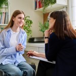 Smiling young teenage female patient talking to a female therapist
