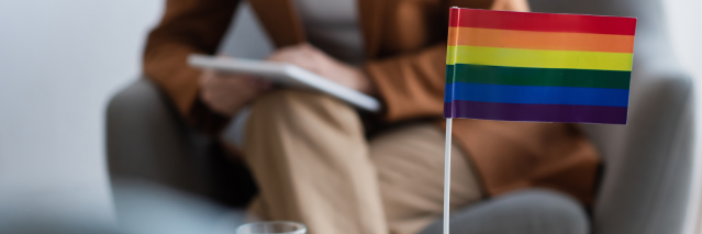 Counselor sitting on couch behind a Pride flag