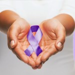 Healthcare and social problems concept - close up of woman hands holding purple domestic violence awareness ribbon over violet background