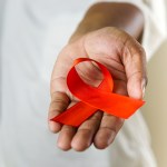 A hand holding a red ribbon, symbolizing AIDS and HIV awareness, raising support and promoting solidarity with those affected by the illness.