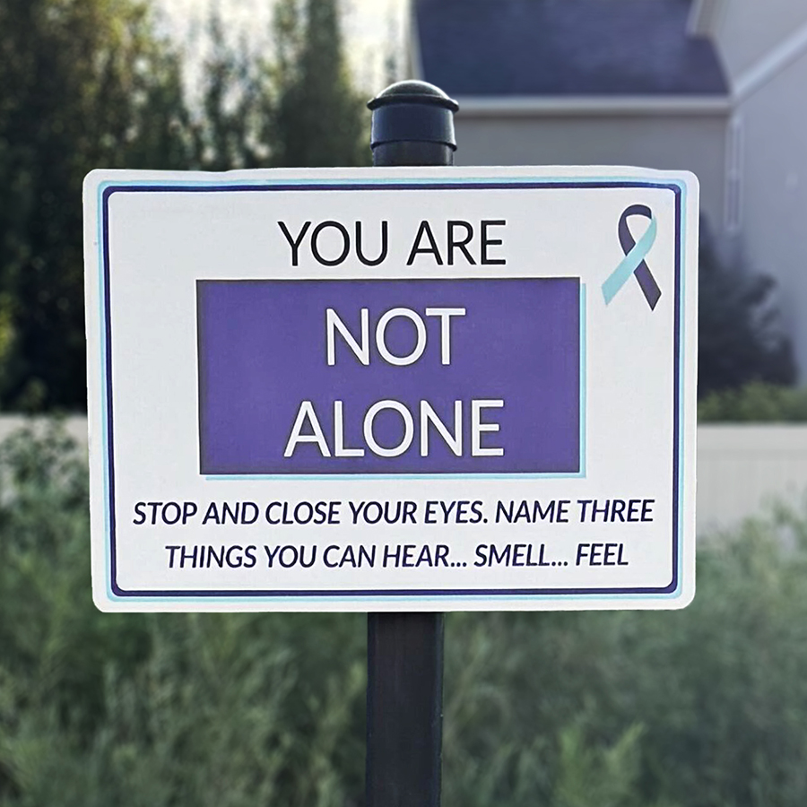 A trail sign that says, "You are not alone. Stop and close your eyes. Name three things you can hear... smell... feel