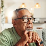 Sad, old man and thinking with cane in home for retirement stress, regret or nostalgia with daydreaming. Lonely, mental health and elderly person with walking stick on sofa for reflection or dementia