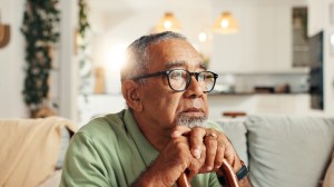 Sad, old man and thinking with cane in home for retirement stress, regret or nostalgia with daydreaming. Lonely, mental health and elderly person with walking stick on sofa for reflection or dementia